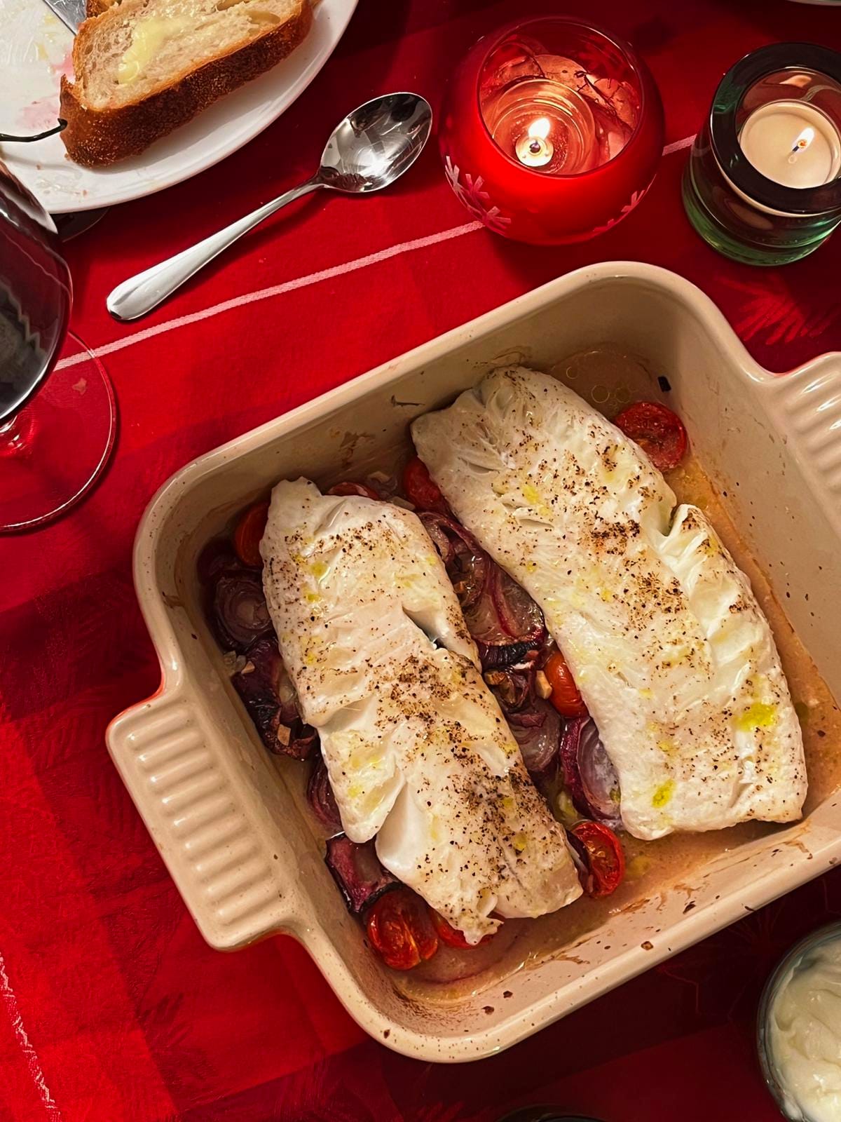 Baked white fish with cherry tomatoes on a red tablecloth