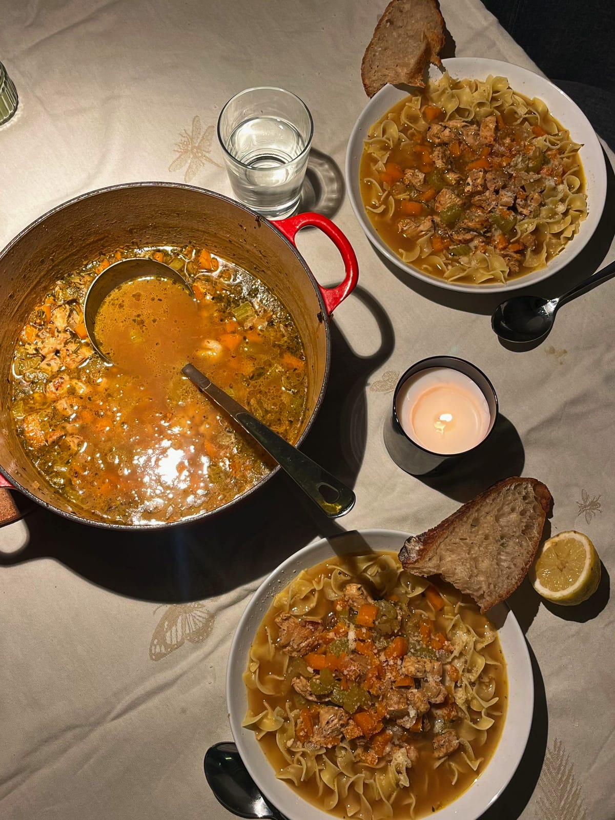 Soup pot, bowls of noodle soup and bread on a candlelit table