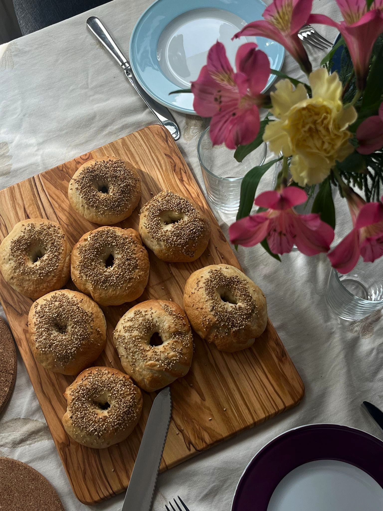 Homemade sesame bagels on an olive wood board with pink flowers